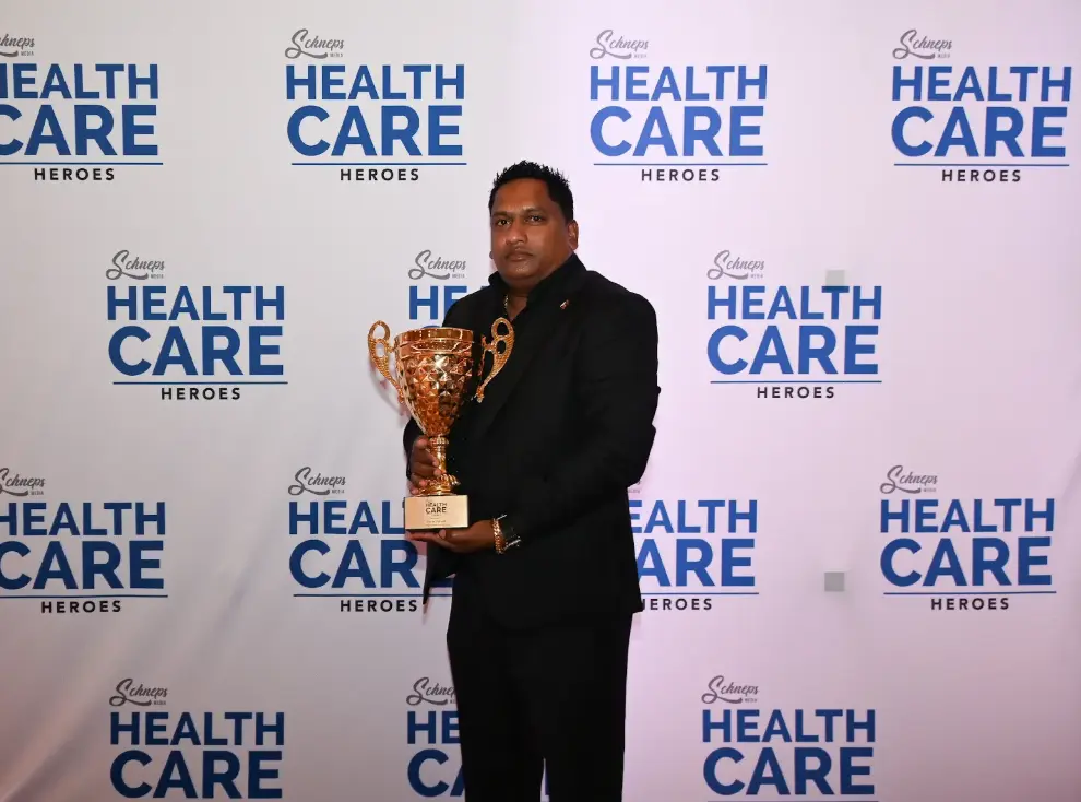 Navin Shivpal with the Health Care Heroes award trophy in front of the event backdrop